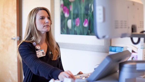 A female radiology/mammogram technologist is looking at a device screen in the breast center.