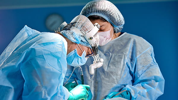 Two surgeons in blue scrubs performing breast reconstruction surgery in a sterile operating room.