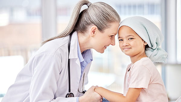 a female doctor smiling and holding hands with a young girl in a hospital room