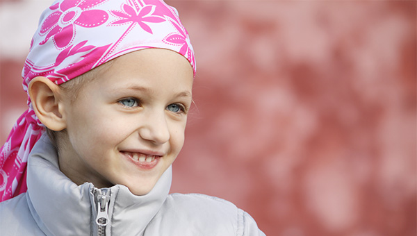 A pediatric cancer patient with a headscarf smiles.