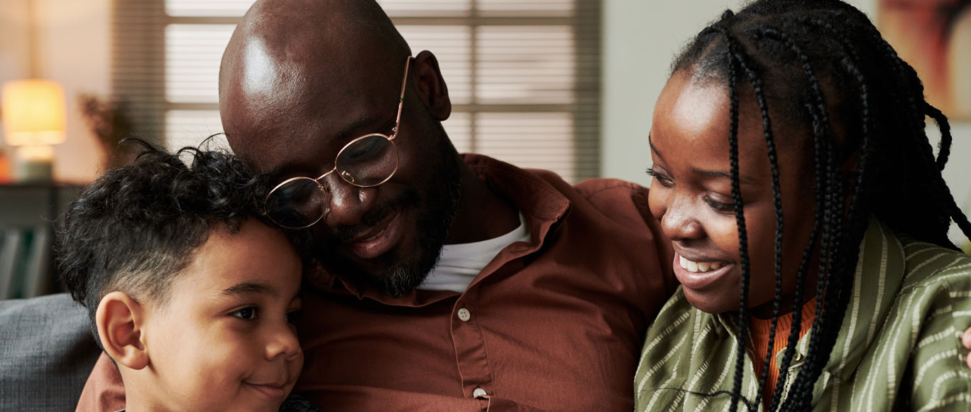 an African American family sitting down hugging each other, with a mom, dad, and young child