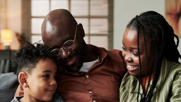 an African American family sitting down hugging each other, with a mom, dad, and young child