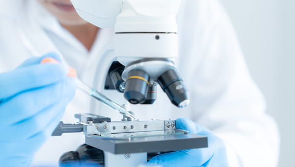 A lab-coated individual studies a microscope, focused on genetic testing related to cancer.