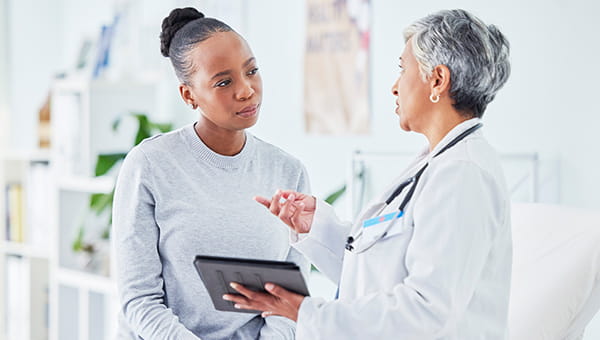 A woman engages with a doctor, holding a tablet, focusing on gynecological cancer care and available treatment programs.