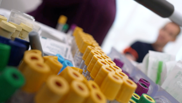 A close-up pf bloodwork collection tubes with a blurred patient in the background.
