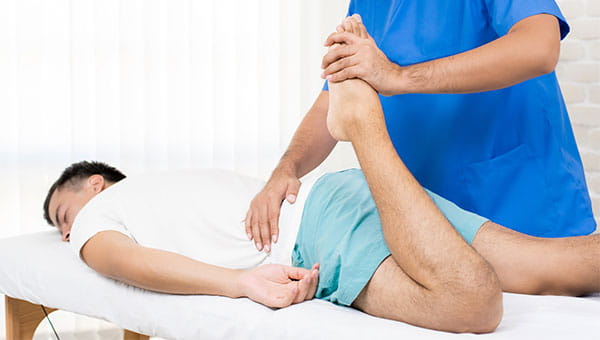 A male physical therapist stretches the left leg of a male patient.