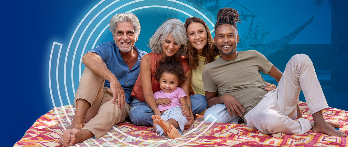 Image of a diverse family sitting together smiling on a picnic blanket. 