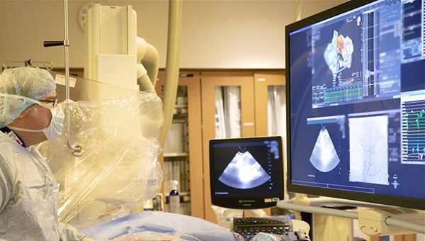 an image from the structural heart and valve clinic at St Joseph's Hospital showing a doctor in scrubs in the surgical room standing above a patient looking at an X ray on the screen