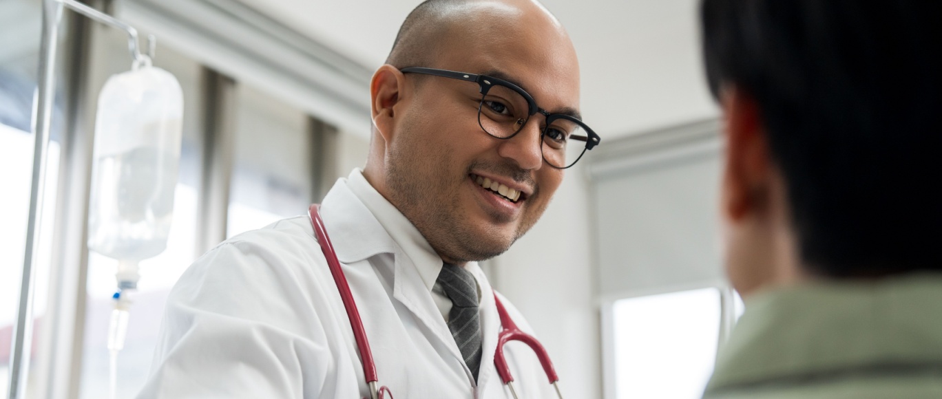 A male cardiologist smiles warmly at a patient during a consultation in a medical office.