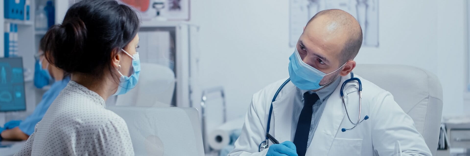 male doctor wearing mask talking to female patient