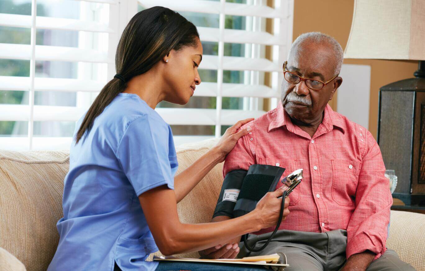 A female nurse checks the blood pressure of an elderly male at home. 
