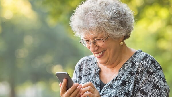 elderly woman smiling looking at her phone outdoors