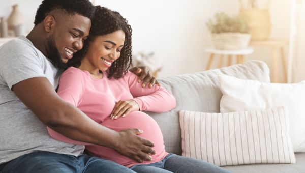 Pregnant couple sitting on a couch smiling.