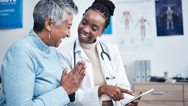 A black, female doctor showing an elderly, black, female patient something on an iPad.