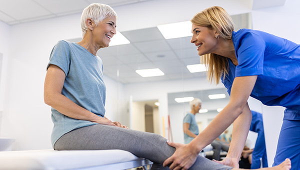 A physical therapist helps to stretch an elderly patient's leg.