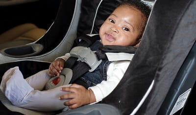 A smiling infant is sitting in his car seat.