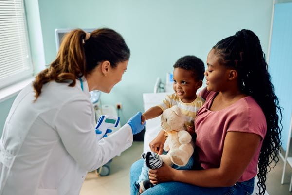 A doctor shaking hands with a child patient, while the child's mother holds him. 