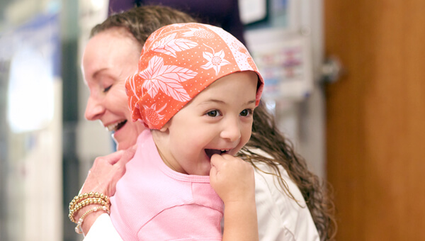 A female pediatric cancer patient hugs a doctor.