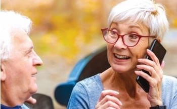 A senior woman is talking on her cellphone while sitting next to her husband.