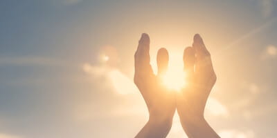 two hands praying and held up to the sky and sun