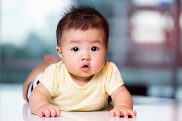 5 months old cute baby girl lying on her stomach, and trying to get the pacifier in front of her