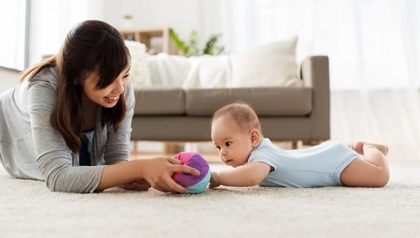 family and motherhood concept happy mother and baby son playing with ball at home