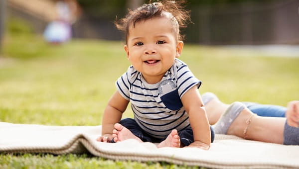 Little baby boy sitting up on a blanket in the park looking to camera close up