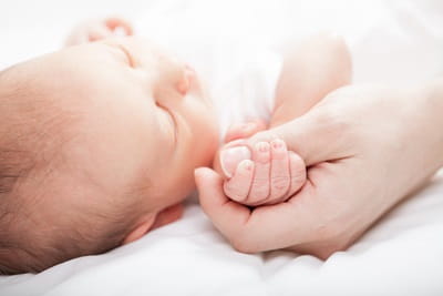 A newborn is holding his mother's thumb