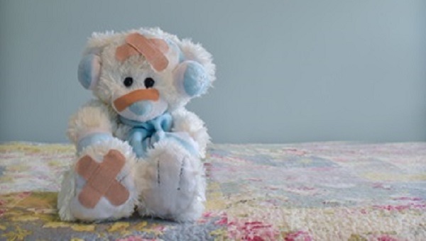 Photo of white bear wearing blue earmuffs and scarf with adhesive bandages on its body