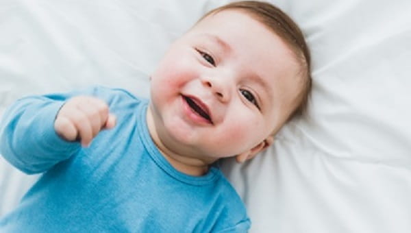 Portrait of an adorable 3 month old baby smiling lying in a bed of white sheets