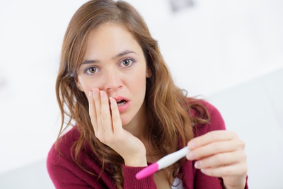 A young woman has a surprised look on her face while holding a home pregnancy test