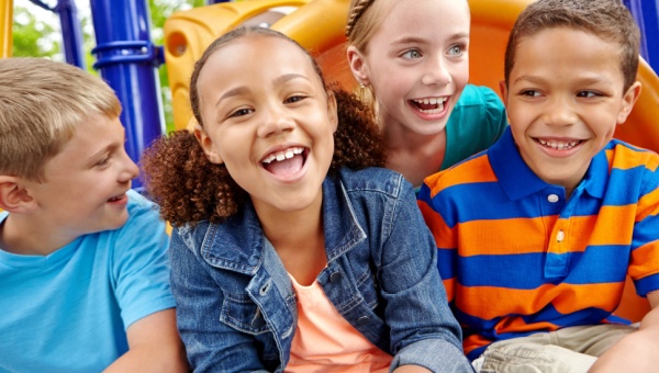 group of four children sitting around on a playground smiling at the camera