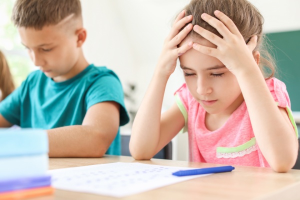 Two children taking a test and one of them has their hands on their head like they are frustrated