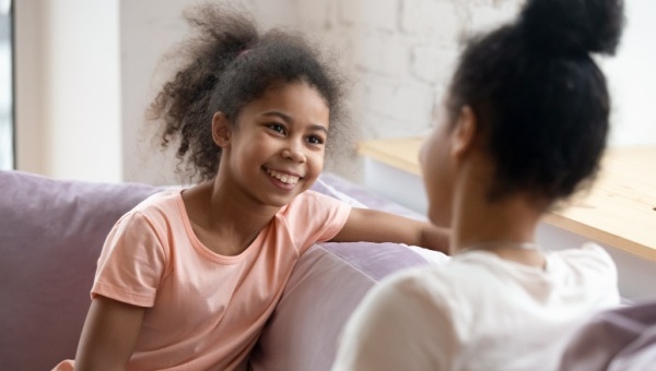 Two young girls are talking to one another while sitting on a couch