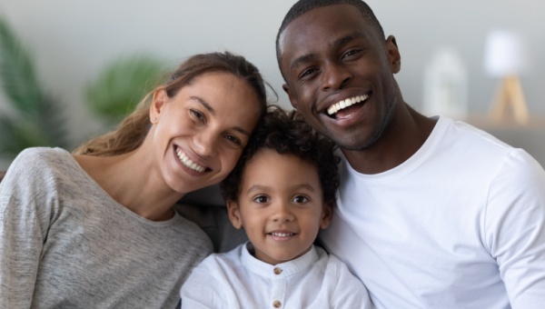 Two parents sitting next to their child looking into the camera and smiling