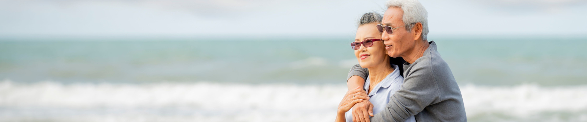 Two senior adults embracing each other along the shore on the beach.