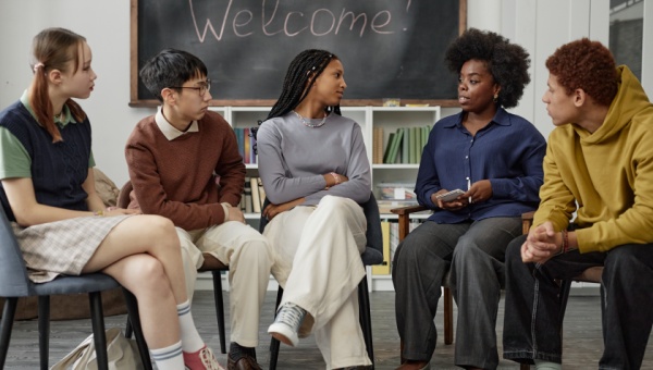 A group of five teenagers sit in a circle and talk.